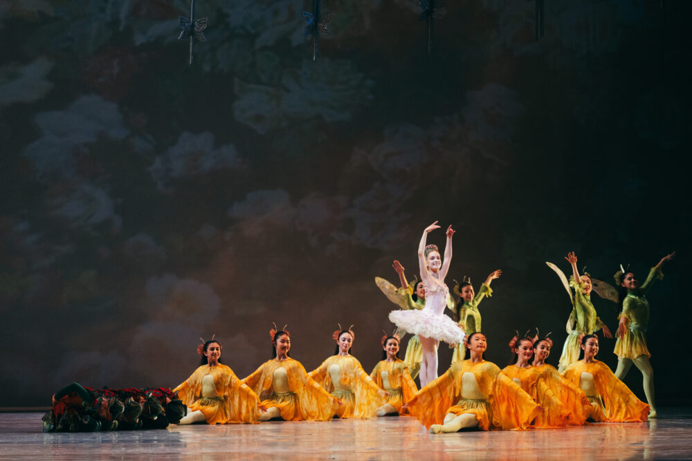 sasha poses in an arabesque w the ballet school students surrounding her dressed as bugs