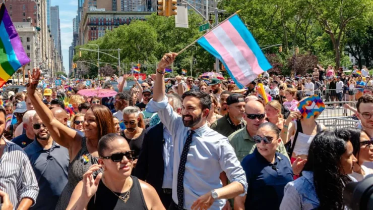 Mamdani showing his support at pride in a sea of rainbows and people, Mamdani holds a trans flag.