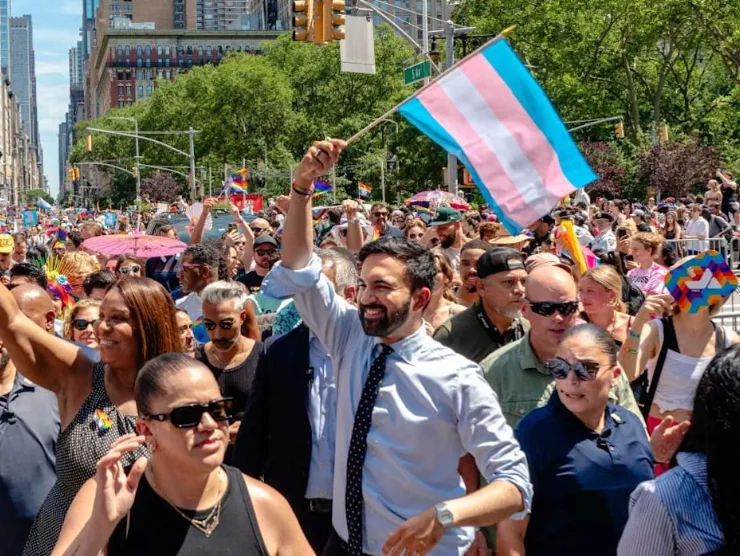 Mamdani showing his support at pride in a sea of rainbows and people, Mamdani holds a trans flag.