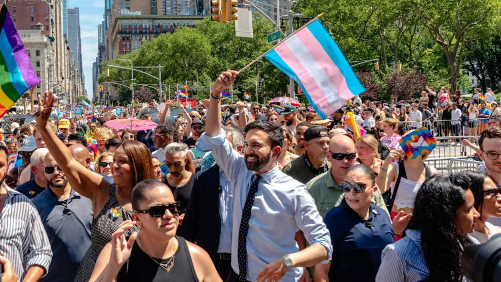 Mamdani showing his support at pride in a sea of rainbows and people, Mamdani holds a trans flag.