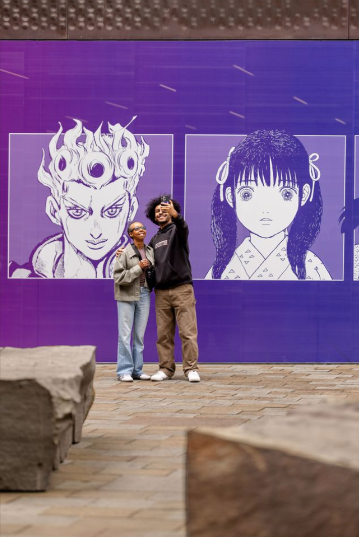 visitors take a selfie in front of the museum with two big manga heads behind them