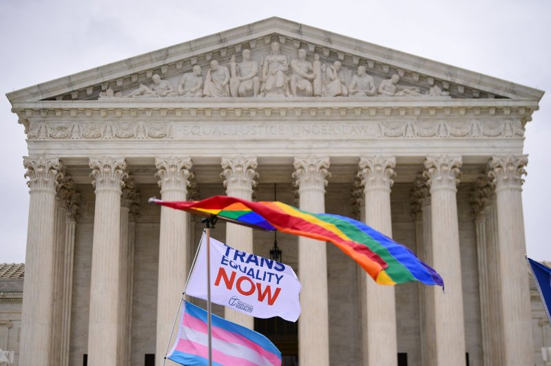 flags waving in front of the supreme court building one rainbow on top and one trans flag on bottom with a flag that says "trans Equality now"