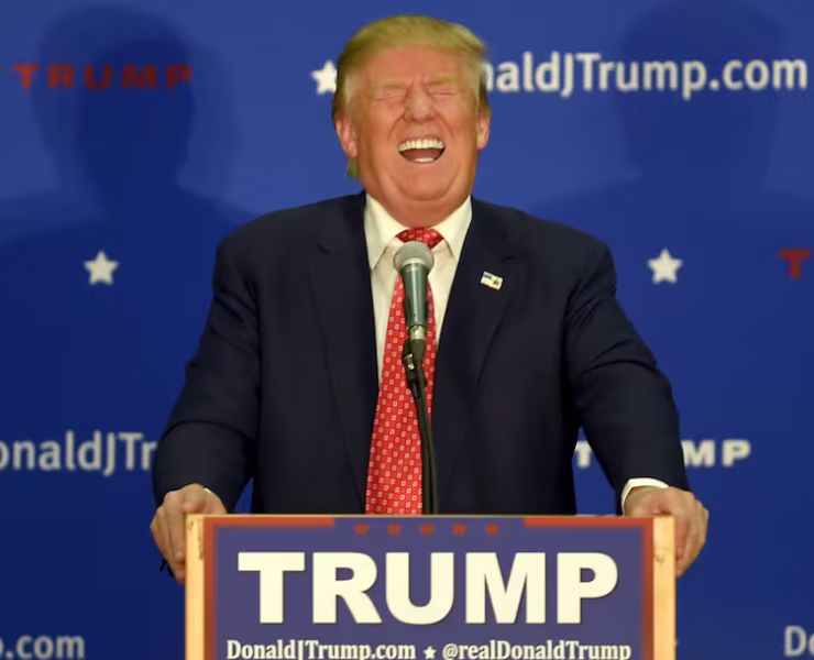 Trump laughing hysterically behind a podium with his name on it