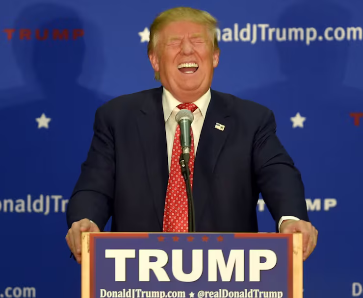 Trump laughing hysterically behind a podium with his name on it